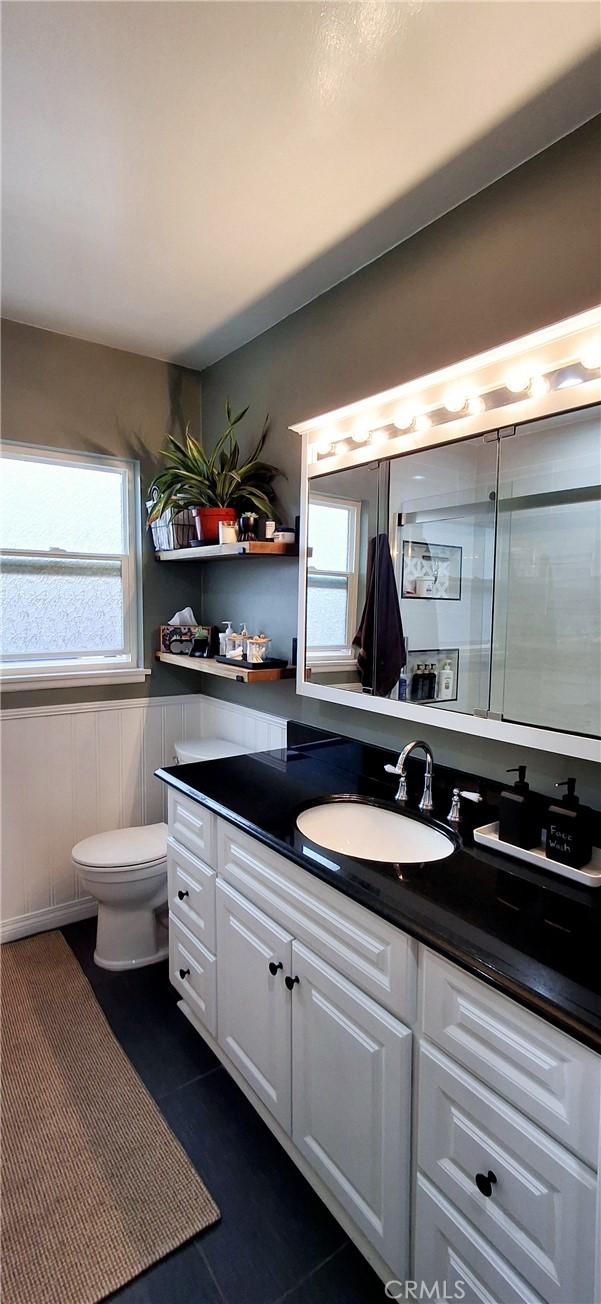 bathroom with toilet, vanity, tile patterned flooring, and a wainscoted wall