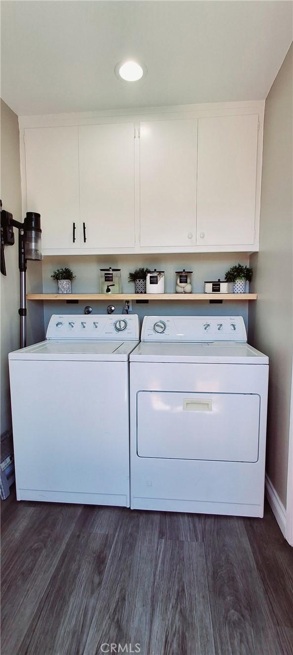 clothes washing area with separate washer and dryer, dark wood finished floors, and cabinet space