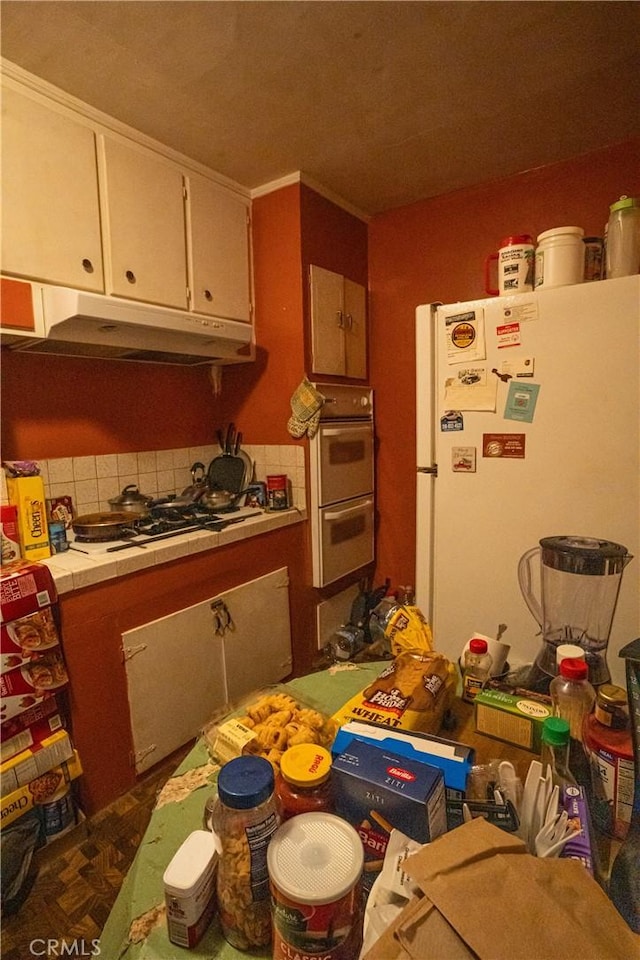 kitchen featuring white cabinets, white appliances, tile countertops, backsplash, and under cabinet range hood