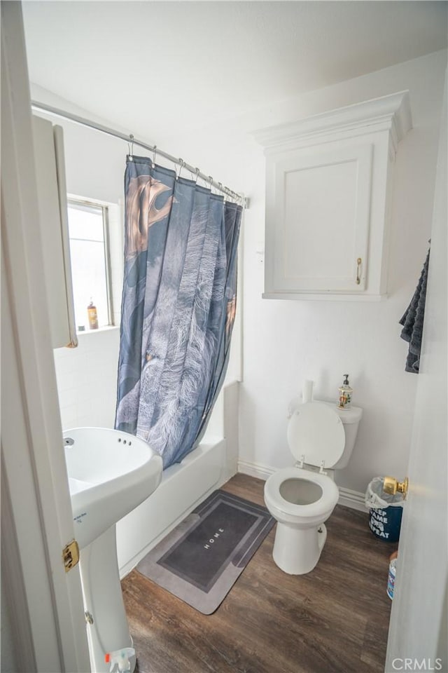 full bath featuring wood finished floors, toilet, baseboards, shower / bathtub combination with curtain, and a sink