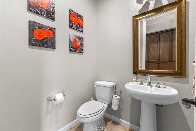 half bathroom with baseboards, a sink, and toilet