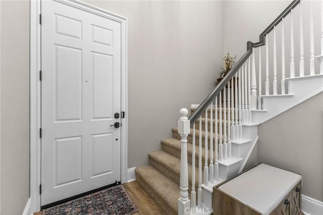 foyer featuring baseboards, wood finished floors, and stairway