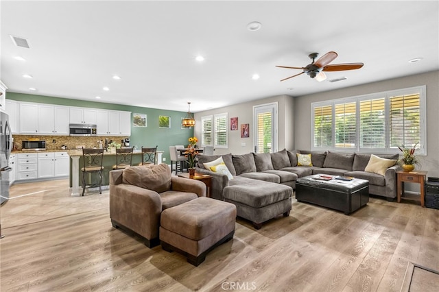 living room with a ceiling fan, light wood finished floors, and visible vents