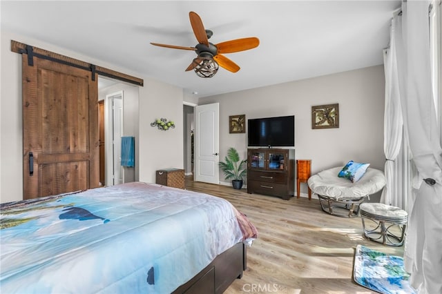 bedroom featuring a ceiling fan, light wood finished floors, and a barn door