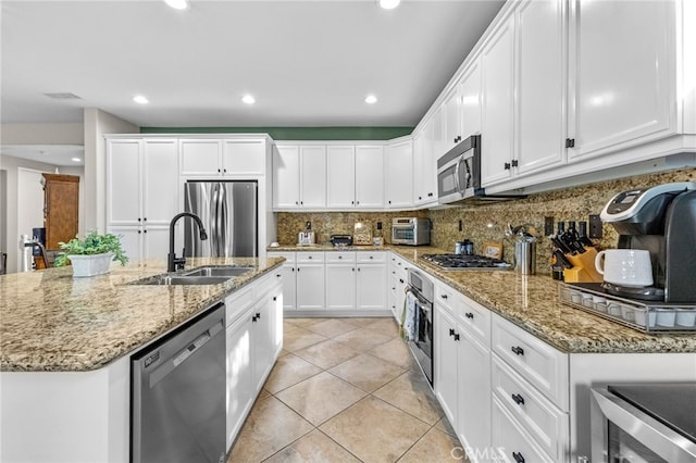 kitchen featuring backsplash, a sink, light tile patterned floors, stainless steel appliances, and white cabinetry