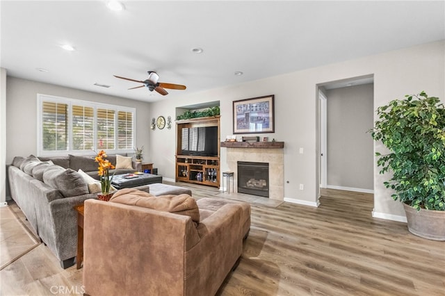 living room featuring baseboards, a fireplace, a ceiling fan, and light wood-style flooring