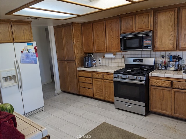 8802 Rubidoux Ave, Yucca Valley, CA 92284 - kitchen with white refrigerator with ice dispenser, stainless steel range with gas stovetop, black microwave, decorative backsplash, and tile countertops