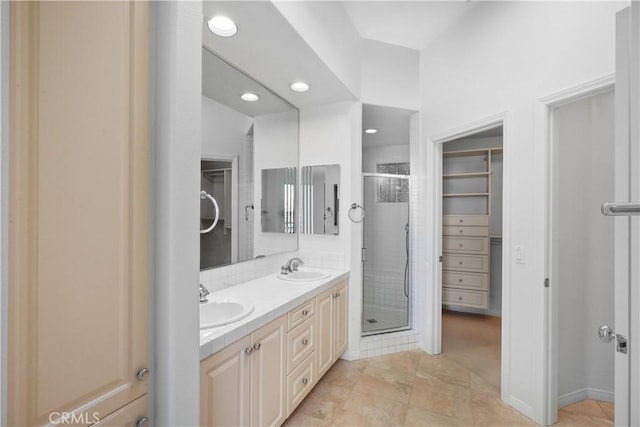 full bath featuring a sink, double vanity, a stall shower, recessed lighting, and a walk in closet