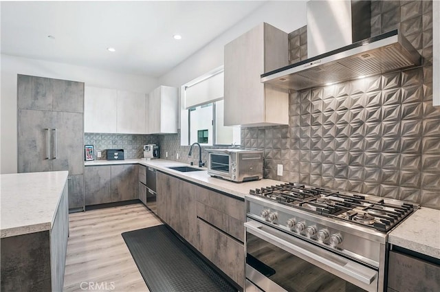 kitchen featuring a toaster, wall chimney range hood, a sink, high end range, and light wood finished floors