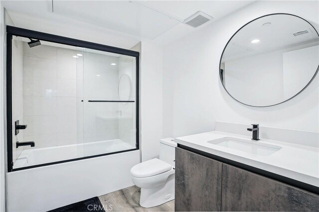 bathroom featuring visible vents, wood finished floors, vanity, combined bath / shower with glass door, and toilet