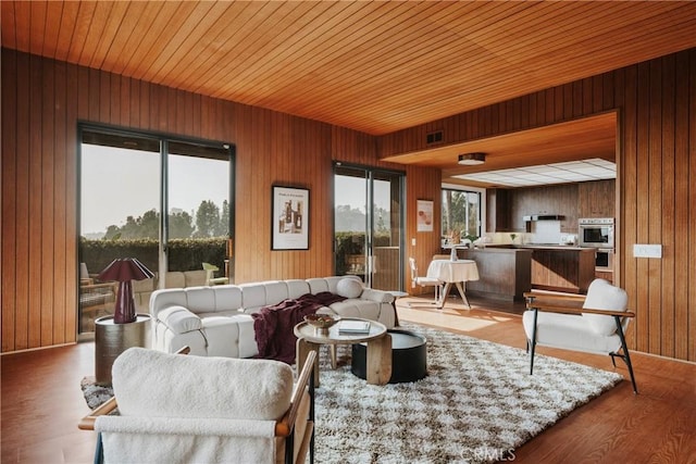 living area featuring wood finished floors, visible vents, wooden walls, and a wealth of natural light