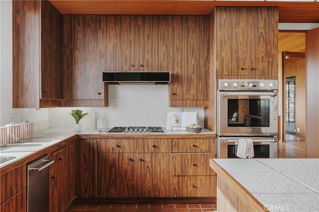kitchen featuring tile counters, stainless steel appliances, tasteful backsplash, extractor fan, and wood ceiling
