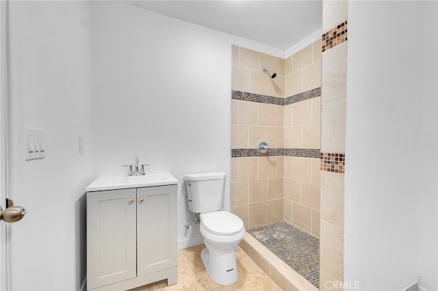 bathroom with vanity, a tile shower, toilet, baseboards, and tile patterned floors