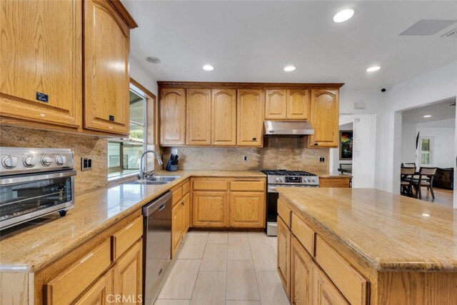 kitchen featuring stainless steel appliances, under cabinet range hood, a toaster, a sink, and light stone countertops