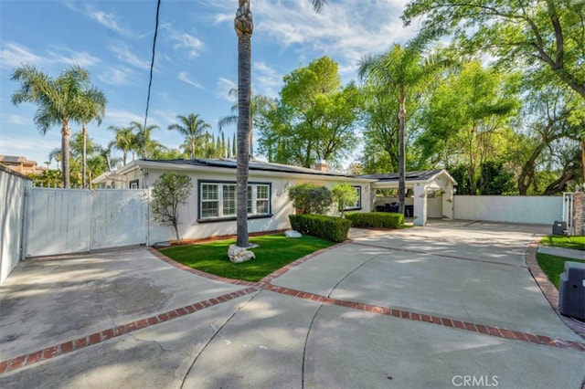 ranch-style house with driveway, a gate, stucco siding, fence, and roof mounted solar panels