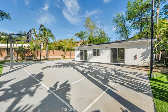 rear view of property featuring stucco siding, fence, and basketball hoop