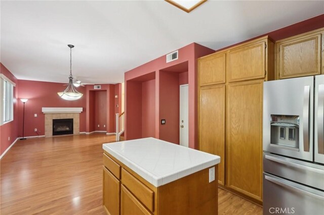 42042 Chestnut Dr, Temecula, CA 92591 - kitchen featuring light wood-style flooring, visible vents, stainless steel refrigerator with ice dispenser, tile counters, and a fireplace
