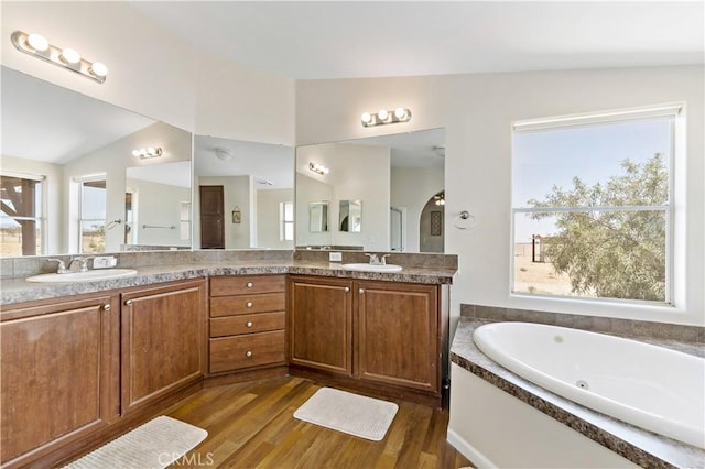 bathroom with lofted ceiling, a tub with jets, a sink, double vanity, and wood finished floors