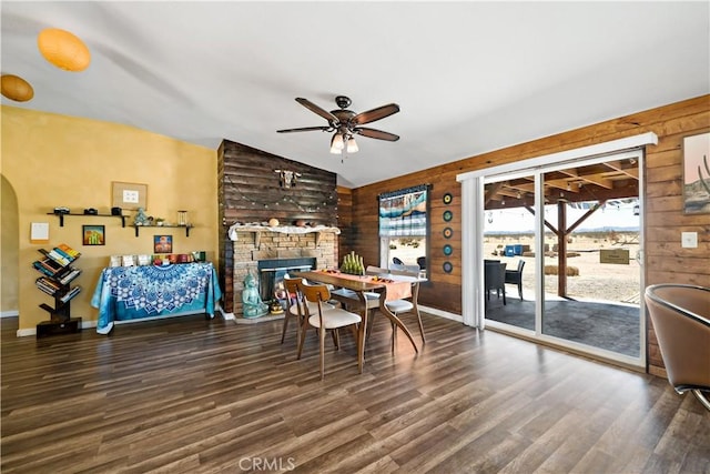 dining space featuring a stone fireplace, vaulted ceiling, wood finished floors, and a ceiling fan