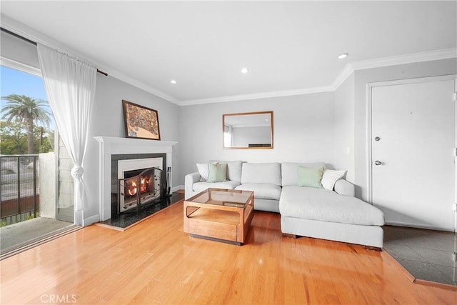 living area featuring crown molding, recessed lighting, baseboards, a warm lit fireplace, and wood finished floors