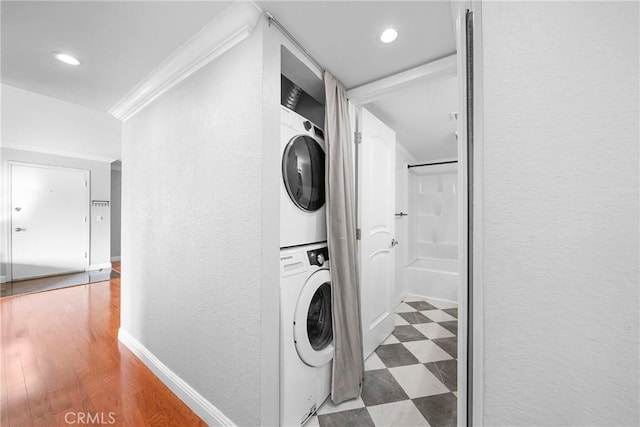 laundry area featuring a textured wall, baseboards, tile patterned floors, stacked washer / dryer, and laundry area