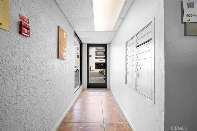 corridor featuring baseboards, tile patterned flooring, a textured wall, and a drop ceiling