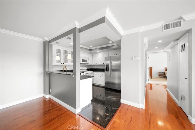 kitchen with white cabinets, visible vents, a peninsula, white appliances, and dark countertops