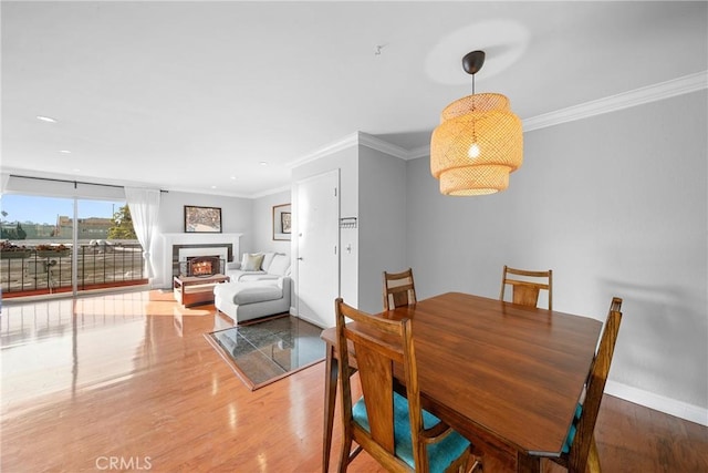 dining area with a warm lit fireplace, crown molding, baseboards, and wood finished floors