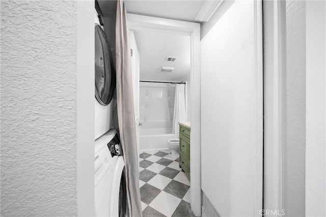 hallway with tile patterned floors, stacked washing maching and dryer, and a textured wall