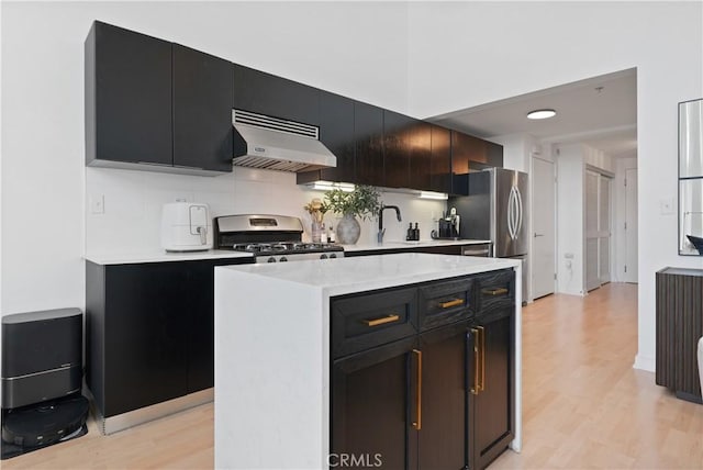 4215 Glencoe Ave Unit 407, Marina Del Rey, CA 90292 - kitchen featuring light wood finished floors, tasteful backsplash, dark cabinetry, appliances with stainless steel finishes, and under cabinet range hood