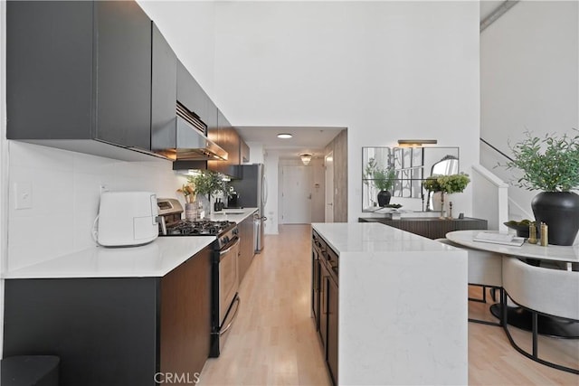 4215 Glencoe Ave Unit 407, Marina Del Rey, CA 90292 - kitchen with light countertops, a towering ceiling, under cabinet range hood, stainless steel gas range oven, and light wood-type flooring