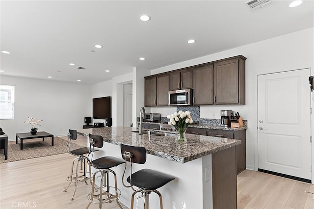 kitchen featuring dark brown cabinets, a sink, light wood-style flooring, stainless steel microwave, and visible vents