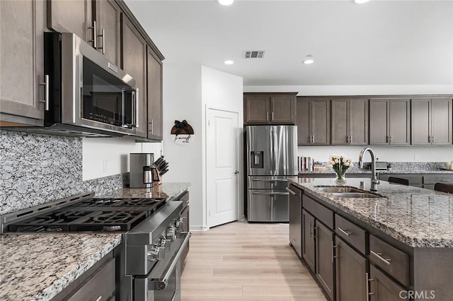 kitchen featuring light stone counters, a sink, dark brown cabinetry, stainless steel appliances, and visible vents