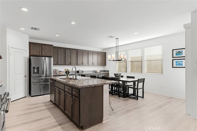 kitchen featuring stainless steel appliances, visible vents, a sink, dark brown cabinetry, and light wood-style flooring