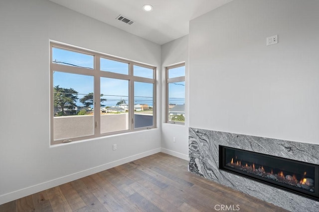 unfurnished living room with baseboards, visible vents, wood finished floors, and a premium fireplace