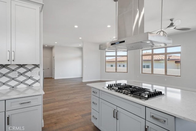 kitchen with stainless steel gas cooktop, wood finished floors, island range hood, decorative backsplash, and recessed lighting