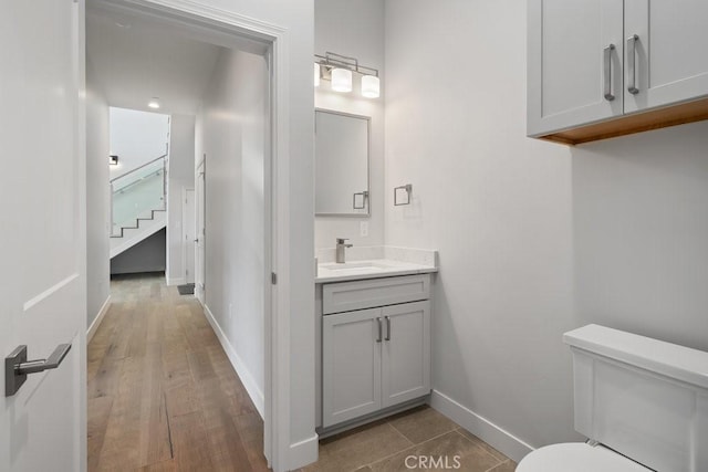 bathroom featuring baseboards, wood finished floors, toilet, and vanity