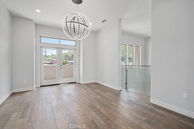 unfurnished dining area featuring visible vents, a healthy amount of sunlight, a chandelier, and wood finished floors