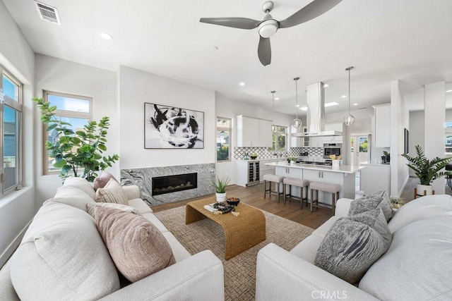 living room featuring a fireplace, beverage cooler, visible vents, ceiling fan, and dark wood-type flooring