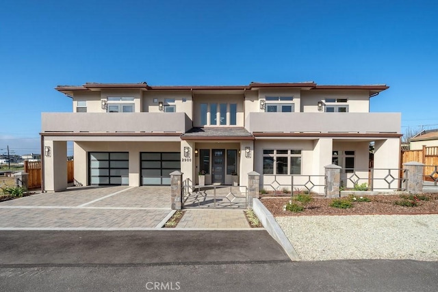 view of front of house with stucco siding, an attached garage, fence, and decorative driveway