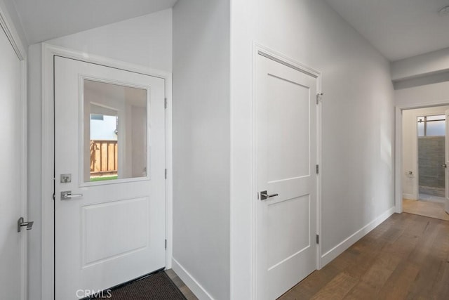 hallway featuring baseboards, wood finished floors, and vaulted ceiling