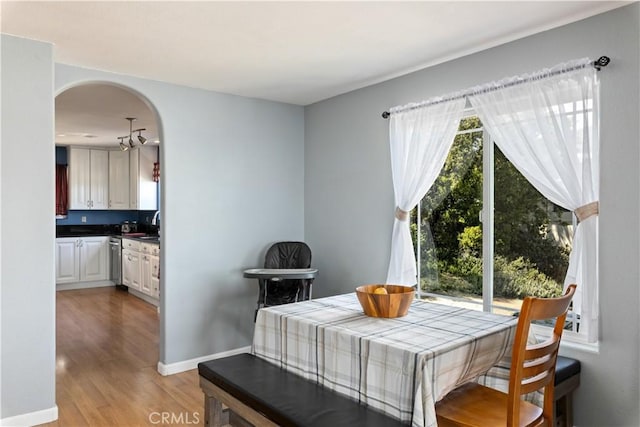 dining space with light wood finished floors, baseboards, and arched walkways