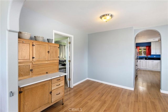 interior space with arched walkways, light countertops, baseboards, and light wood finished floors