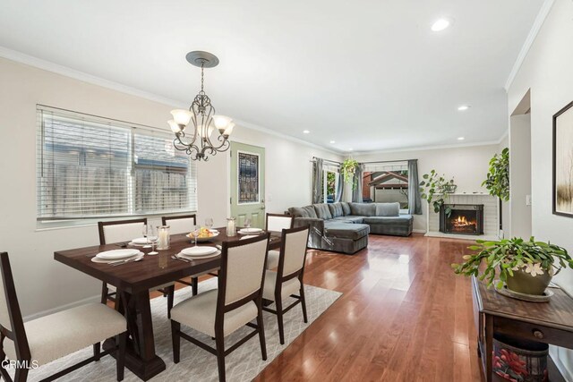dining room with crown molding, a fireplace, wood finished floors, recessed lighting, and a notable chandelier