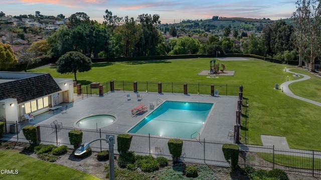 pool at dusk with a patio, fence, a yard, and a community pool