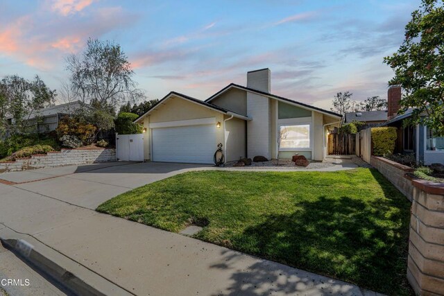 mid-century home featuring an attached garage, fence, concrete driveway, and a front yard