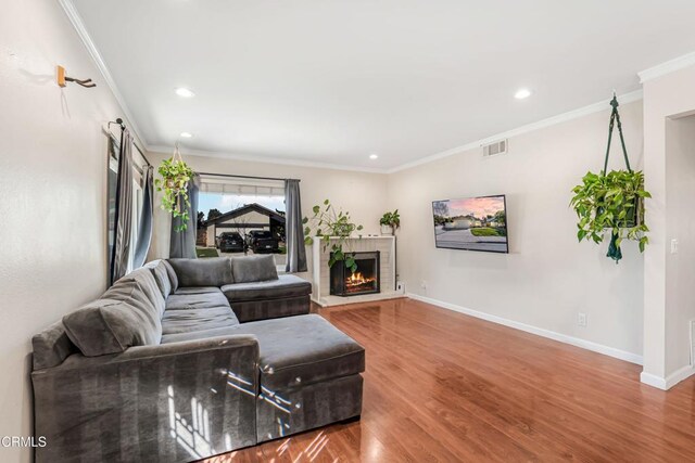 living area with a fireplace, wood finished floors, baseboards, ornamental molding, and recessed lighting
