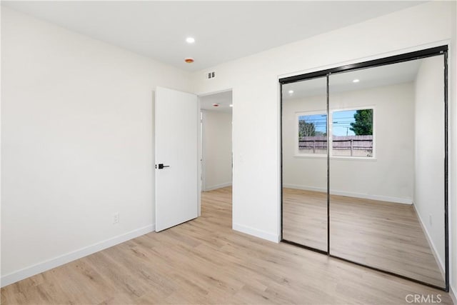 unfurnished bedroom with light wood-style flooring, baseboards, recessed lighting, and a closet