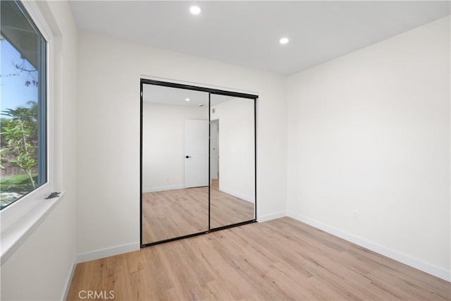 unfurnished bedroom with baseboards, recessed lighting, a closet, and light wood-style flooring