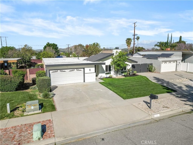 single story home with fence, solar panels, an attached garage, driveway, and a front yard
